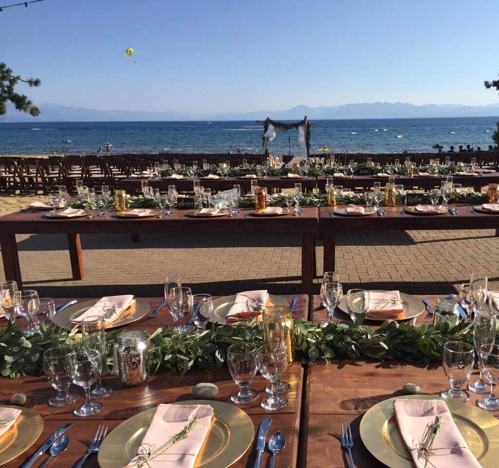 wedding dining area with farm tables set up on terrace in front of lake tahoe