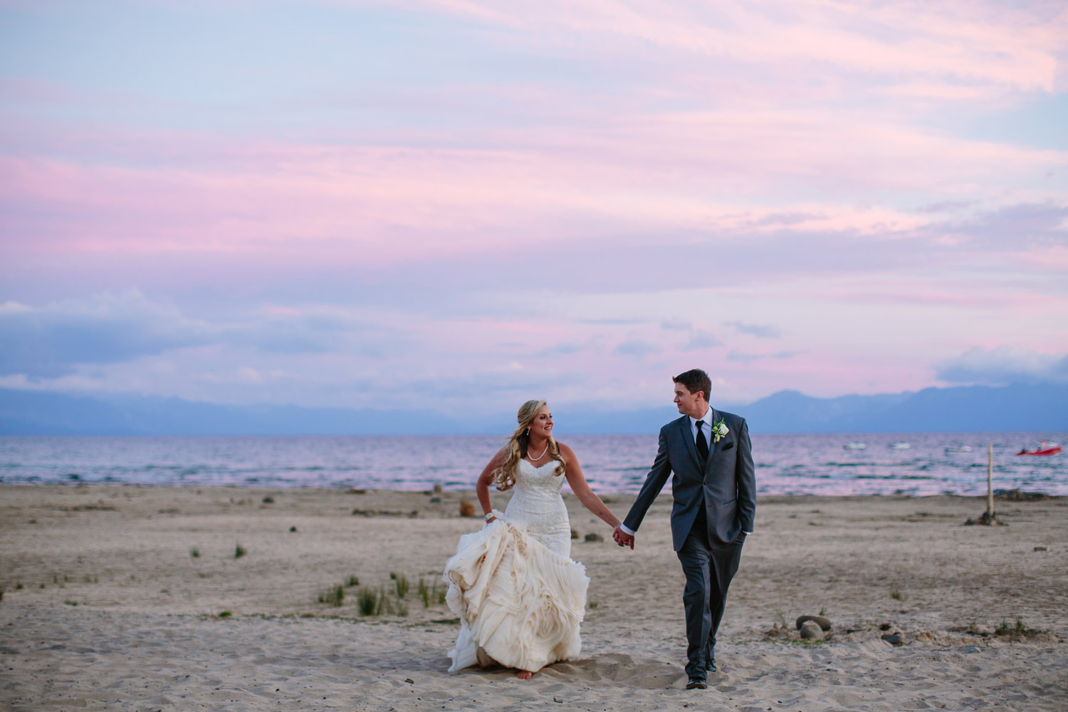 bride and groom walking hand in hand on lake tahoe shore at sunset