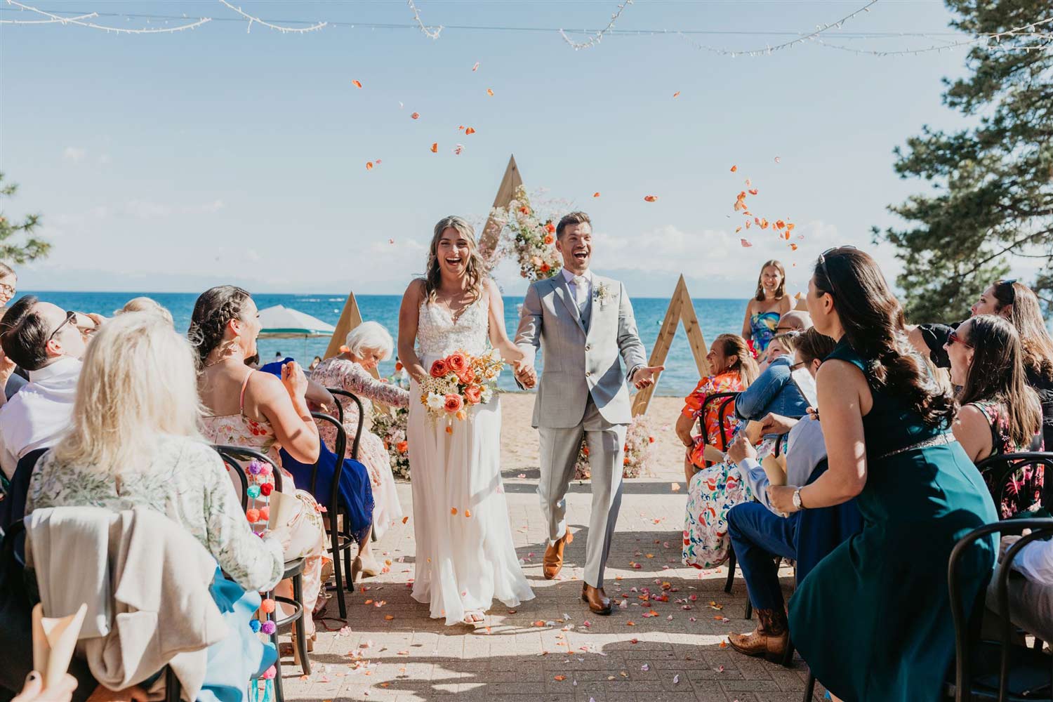 Super happy bride and groom walking down aisle after ceremony with guests throwing confetti