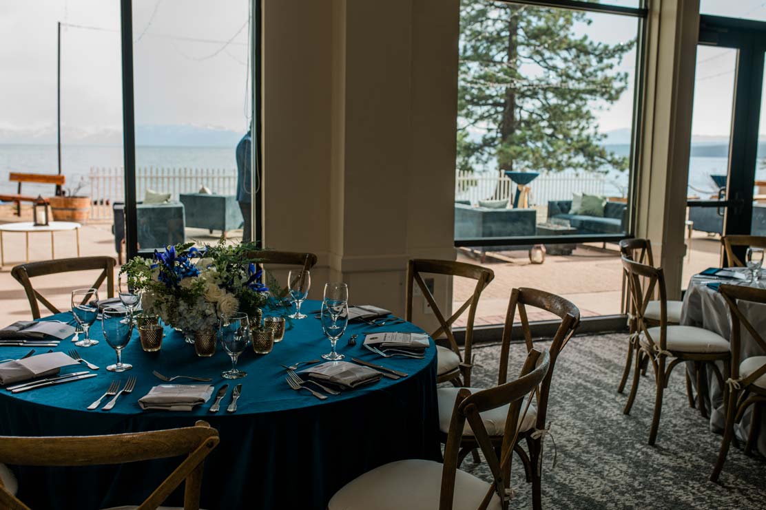 Stunning dining table with royal blue accents placed next to large windows in an event room overlooking terrace and lake tahoe