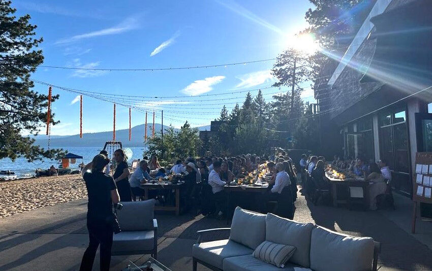 Outdoor dining by the lake on a sunny day with guests enjoying dinner and photographers capturing the moment