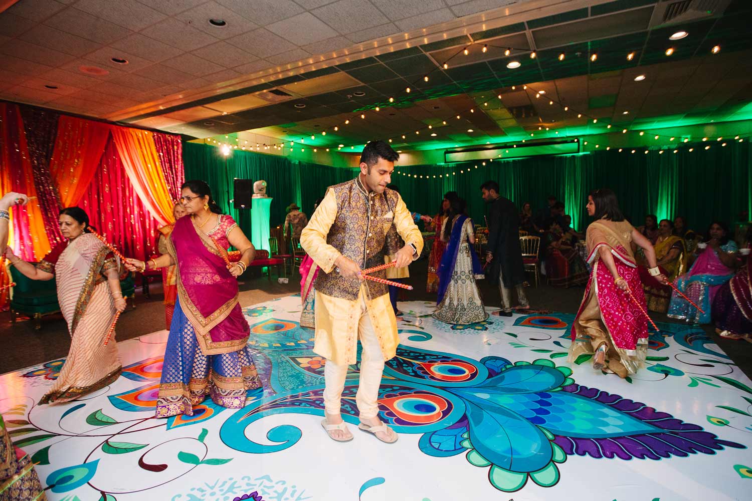 Colorful dance floor with dancers in traditional Indian attire, vibrant lighting, and pink, orange, and green fabric draped on the walls