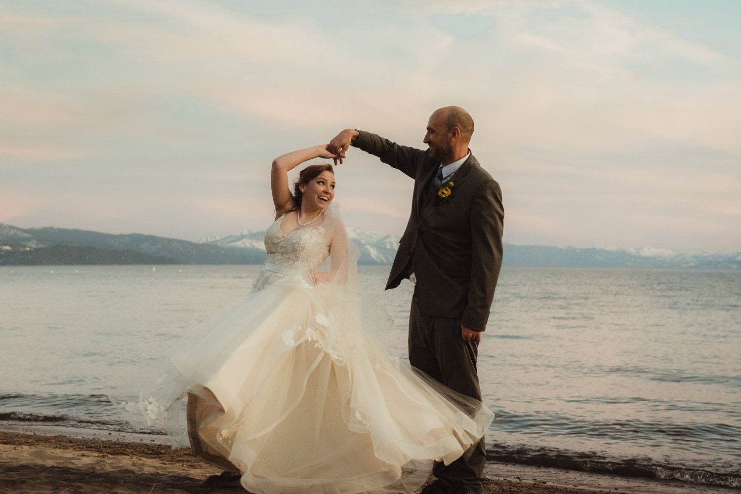 Smiling bride twirling with groom in front of Lake Tahoe at dusk