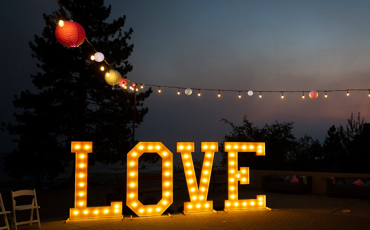 Large illuminated ‘LOVE’ sign at sunset with string lights overhead on a terrace