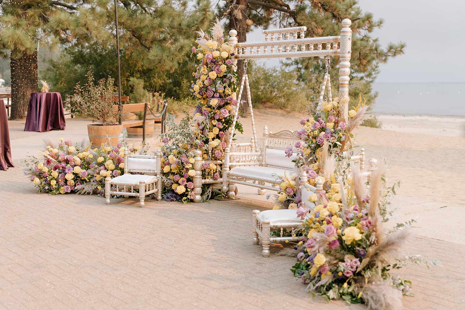 Swing on the beach of Lake Tahoe surrounded by an abundance of yellow and pink flowers, with cocktail tables nearby