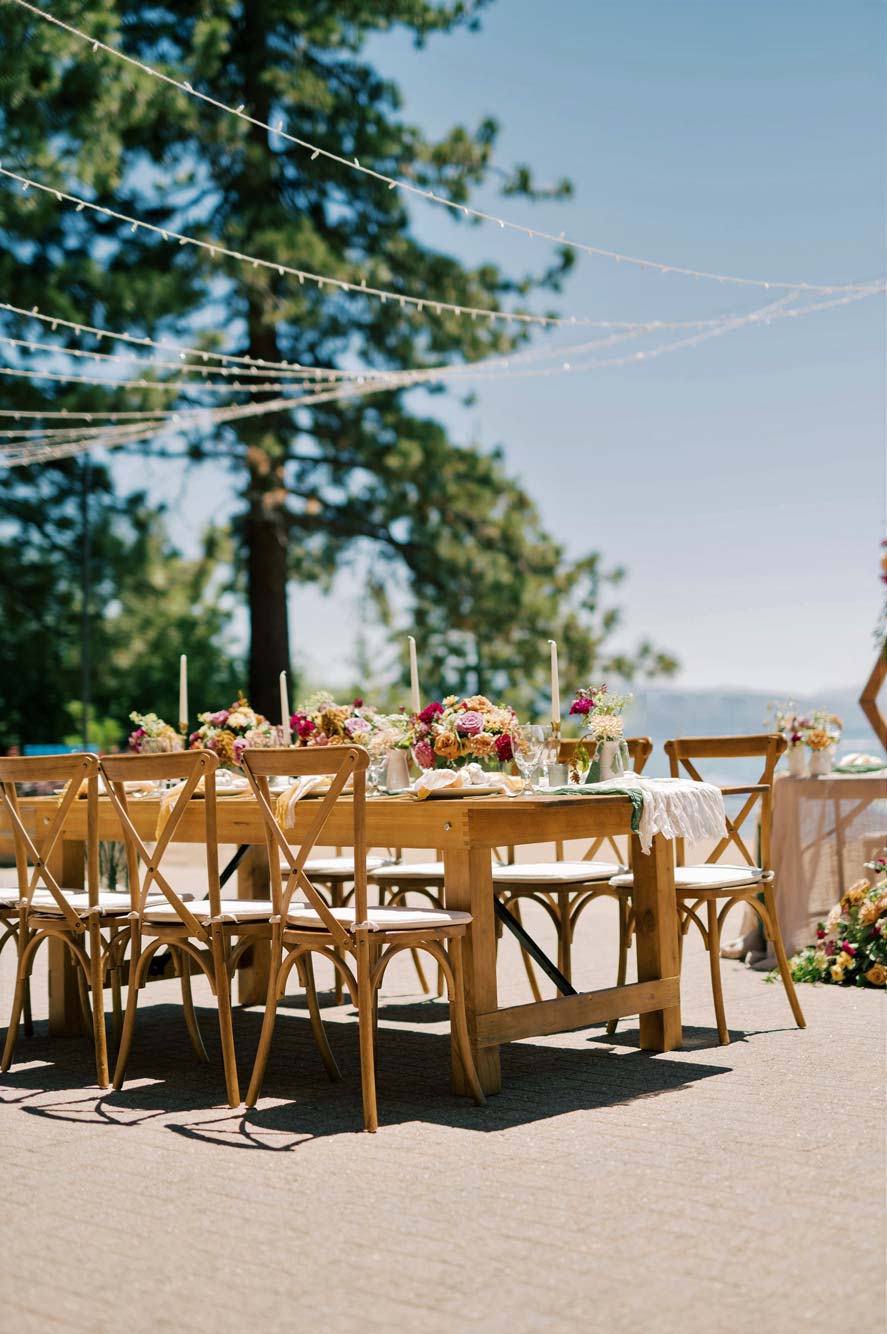 Outdoor wooden tables adorned with fairy lights overhead, floral arrangements, and candles