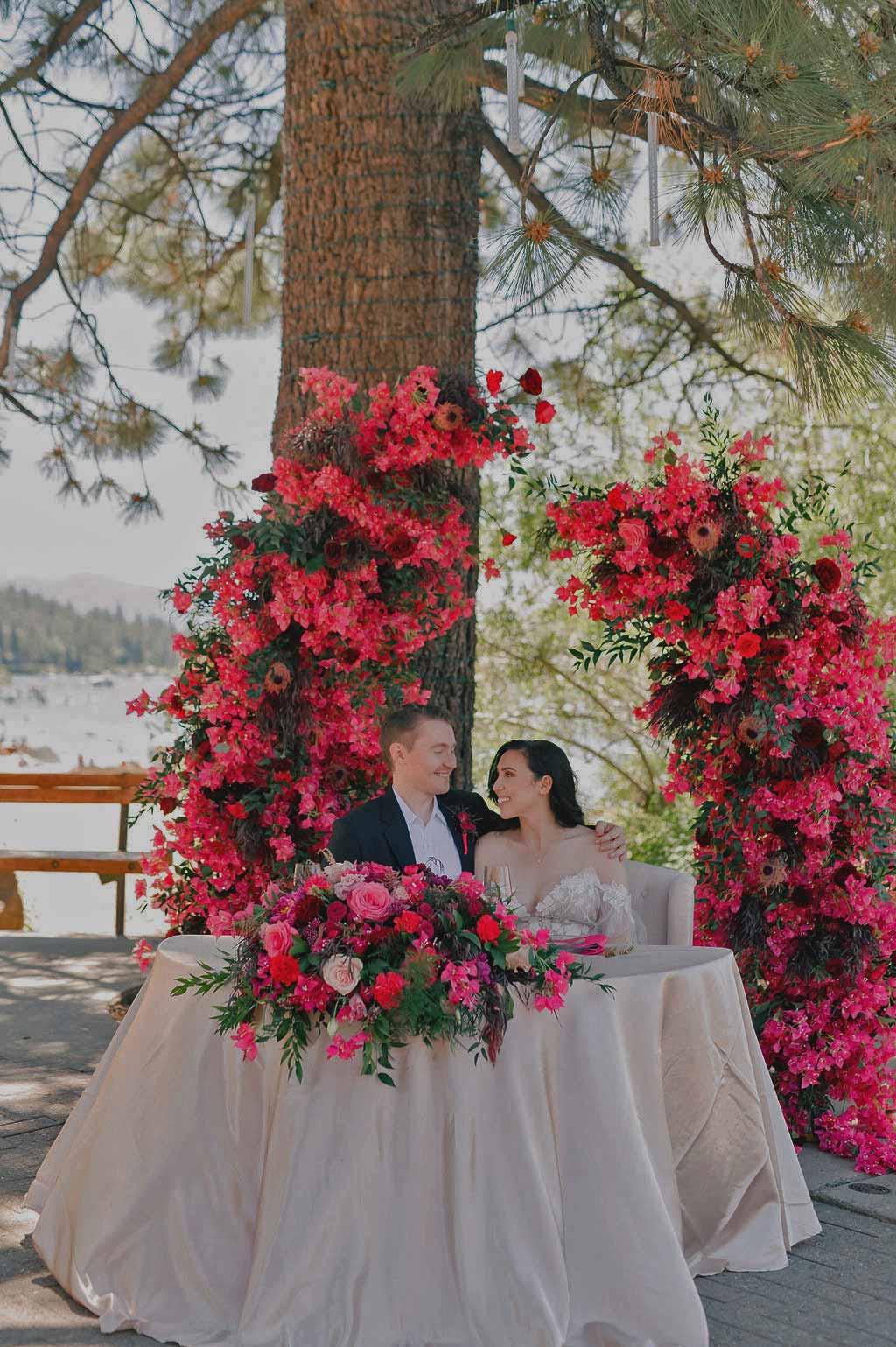 bride and groom in front of floral arch in front of lake tahoe