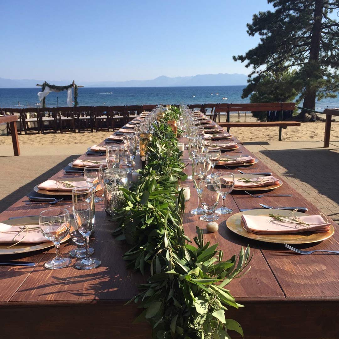 Long farm table set for a wedding on a terrace overlooking a scenic lakefront view